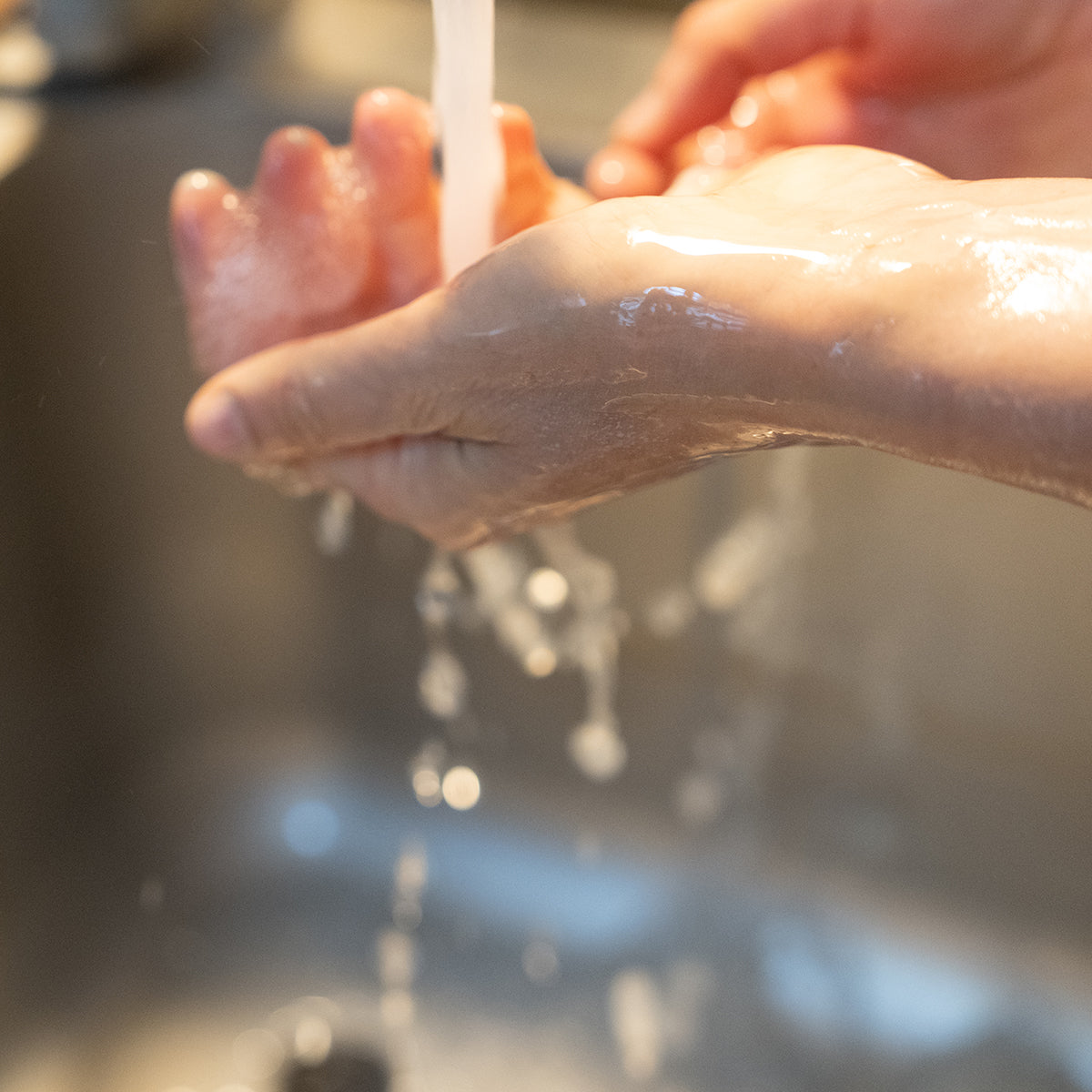 Zwei Hände werden unter einem Wasserstrahl gewaschen.