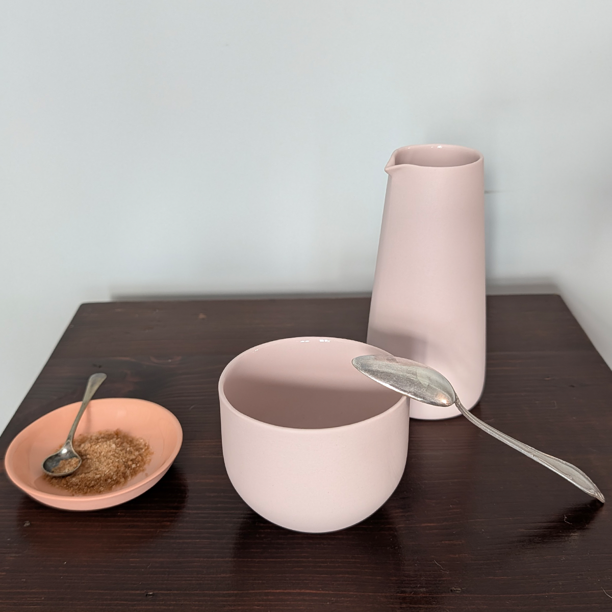 Zartrosa Milchgießer, Kaffeebecher und Tellerchen  aus Porzellan - handgemacht in Berlin, auf einem Holztisch.